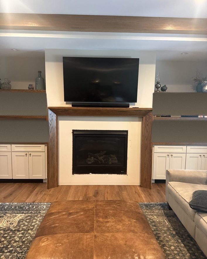 Compound-mitered oak fireplace mantel installed between painted built-in cabinets and open shelving