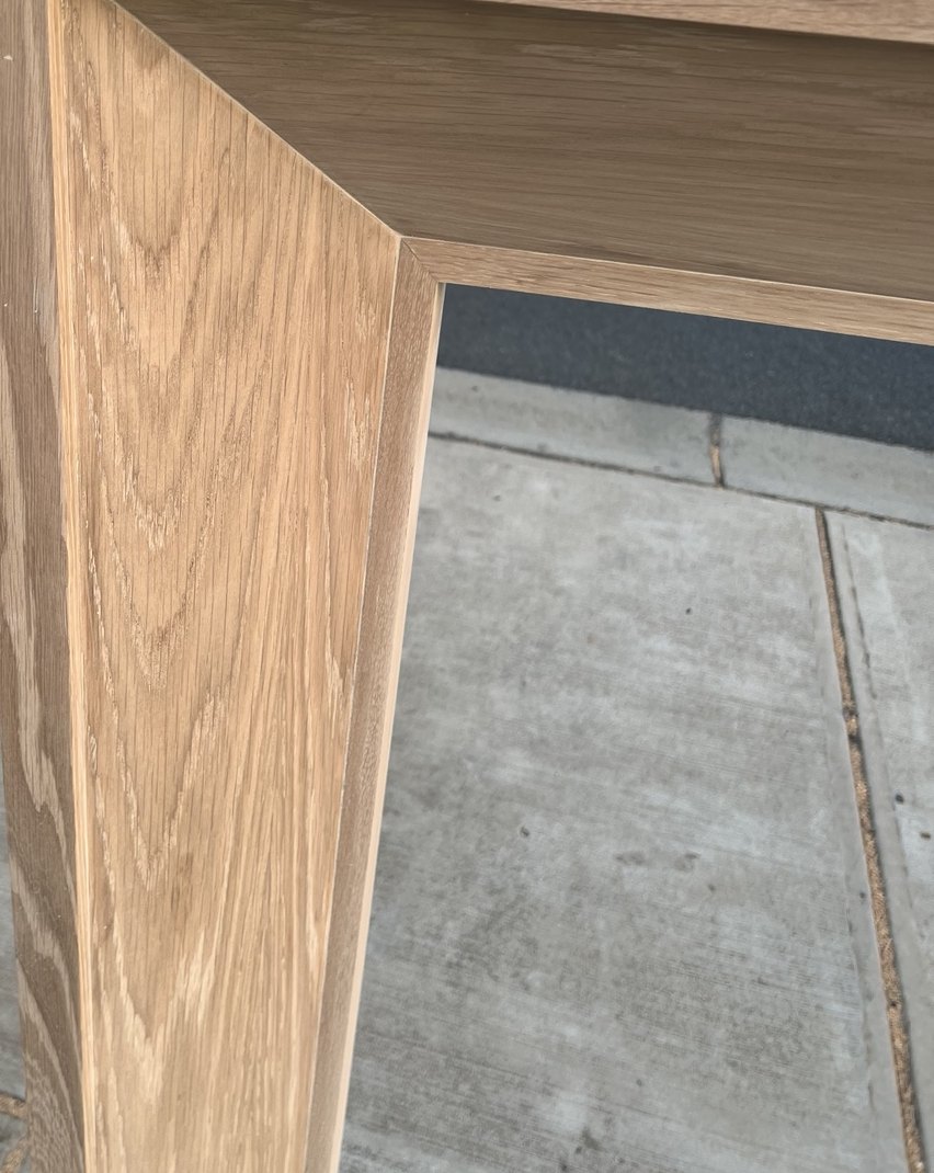 Mitered corner of a solid oak mantel seen from above, the grain meeting cleanly at the joint