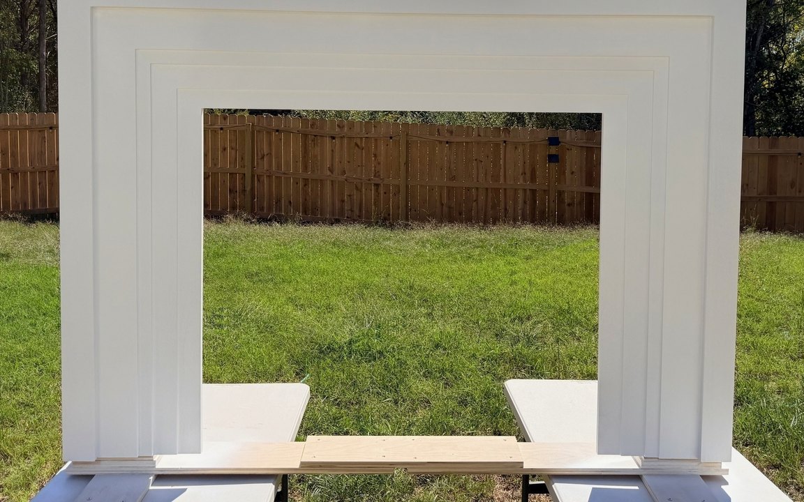The primed mantel surround viewed straight on, its layered trim stepping outward to a deep architectural profile around the opening