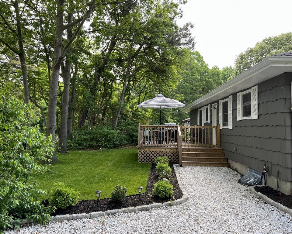 Finished exterior with new siding, a rebuilt deck, gravel path and planted beds